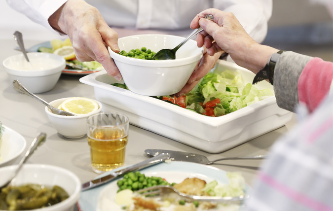 Äldre man tar mat för att lägga upp på sin tallrik vid en måltid på ett äldreboende.